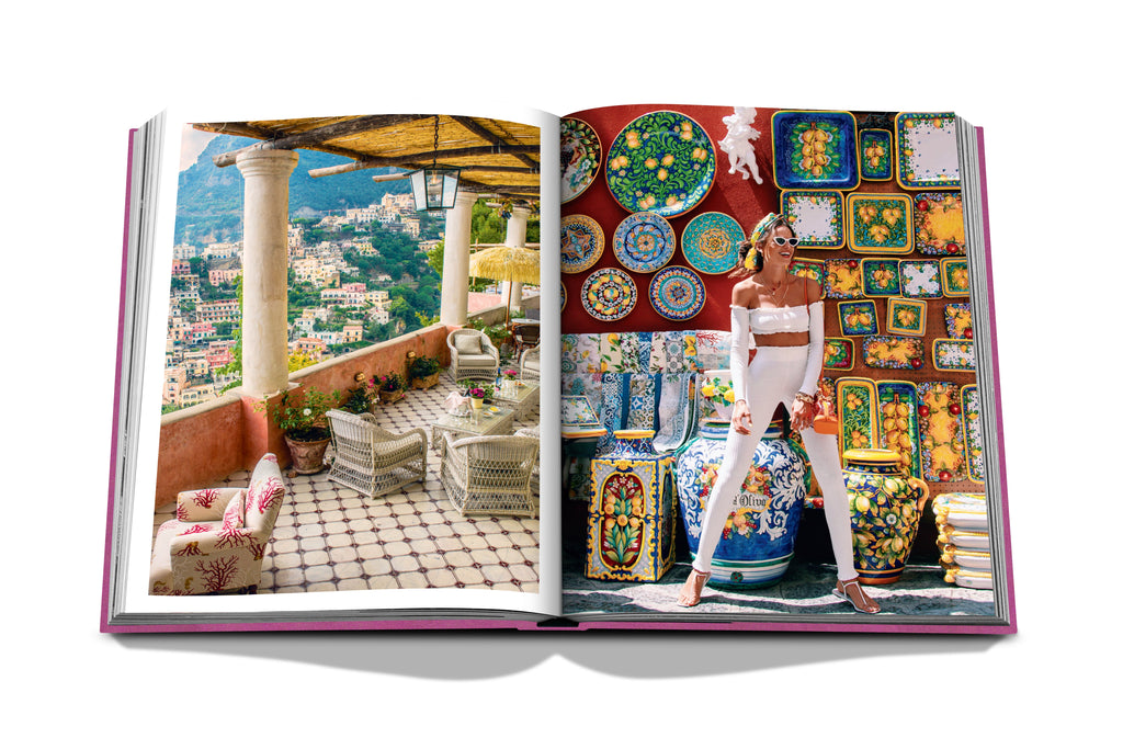 An open book, titled "Amalfi Coast" by Assouline, displays a colorful patio with city views on the left page and a stylish woman posing in front of a vibrant wall adorned with decorative plates, evoking the charming aesthetics found along the Côte Amalfitaine, on the right page.